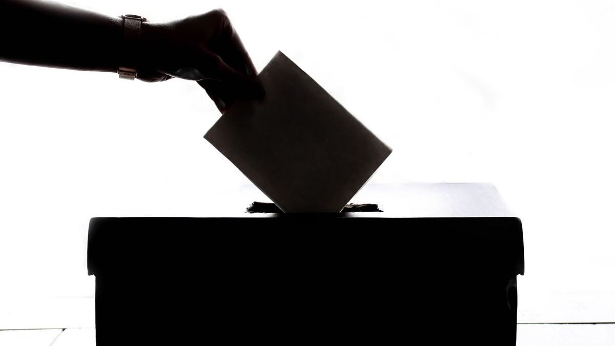 Silhouette of a hand placing a vote into a ballot box