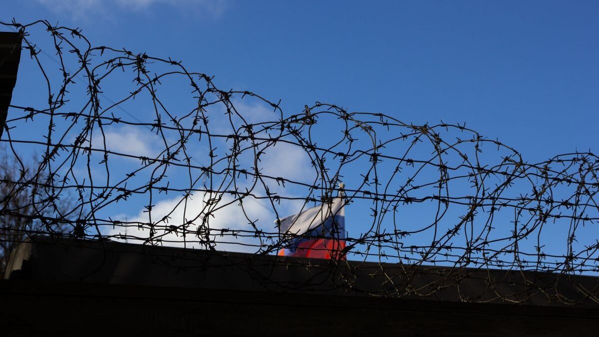 Silhouette of barbed wire with a flag in the background against a clear blue sky