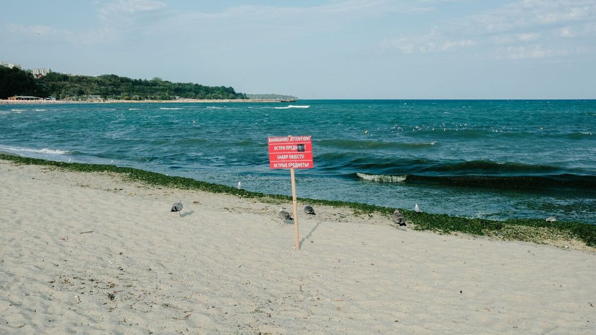 A peaceful beach with a warning sign about sharp objects