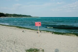 A peaceful beach with a warning sign about sharp objects