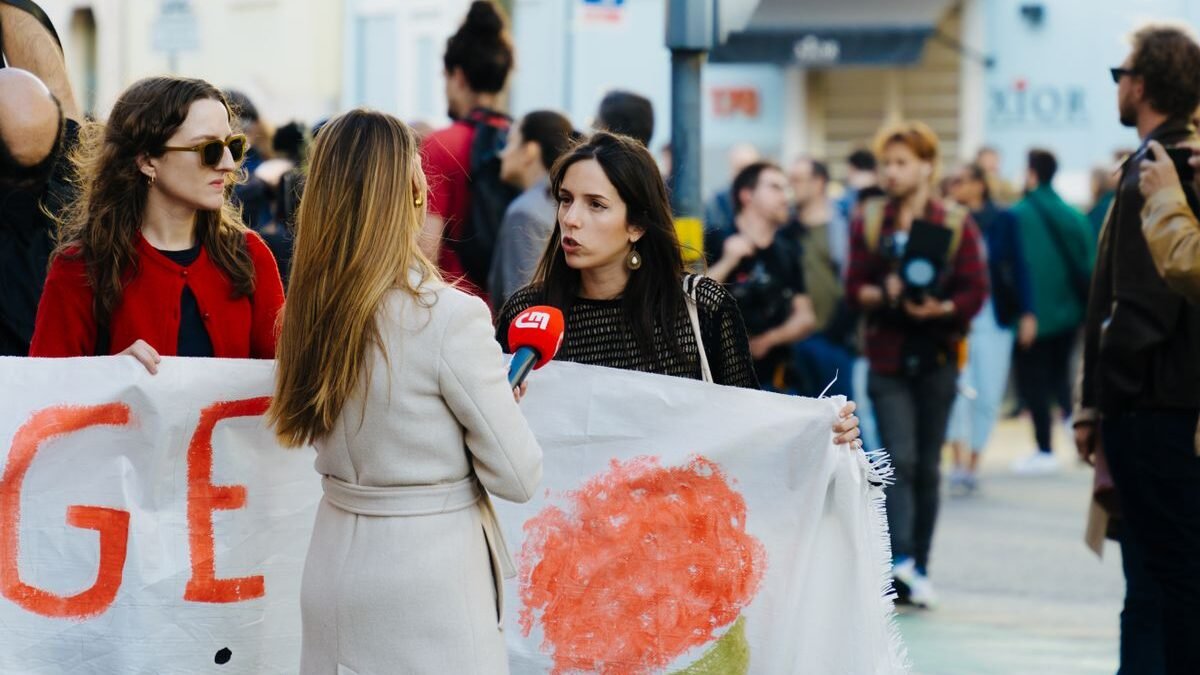 Journalist interviews protesters during a city rally with people holding banners and flags