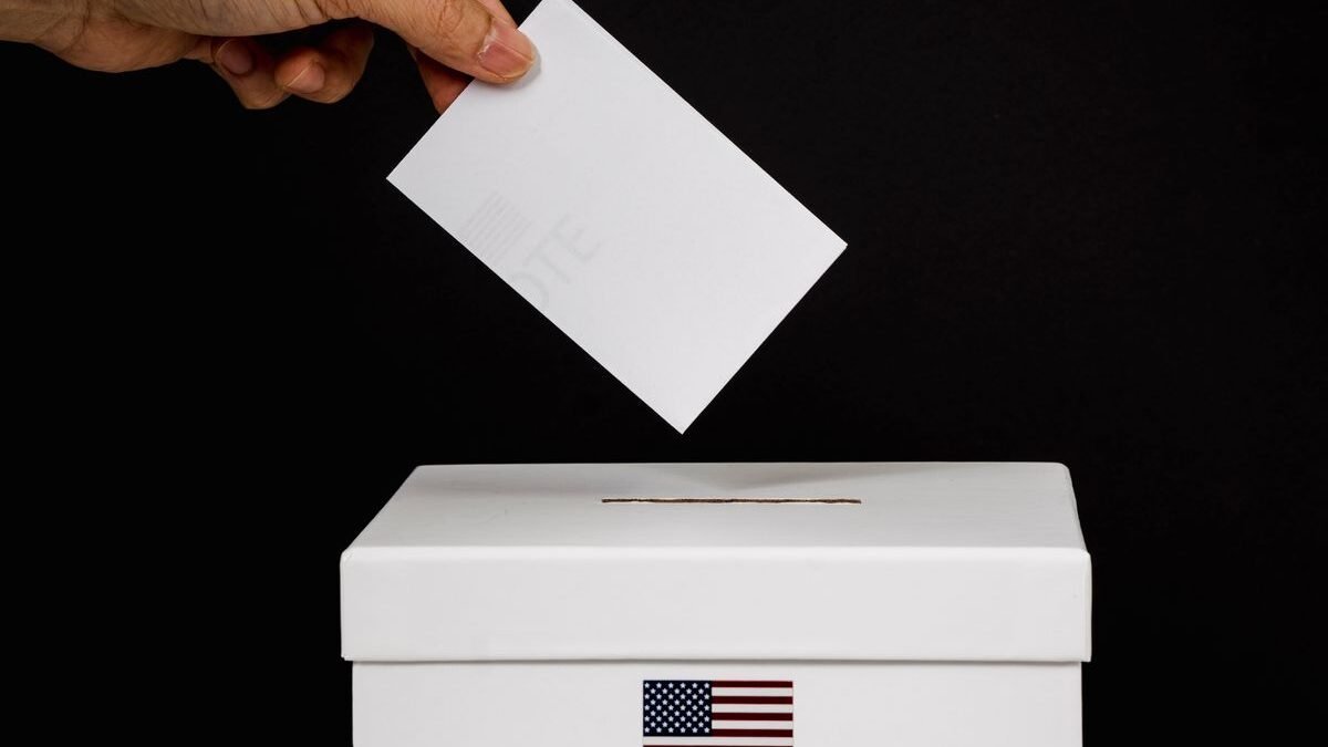 Close-up of a hand placing a ballot into a voting box marked 'Vote'