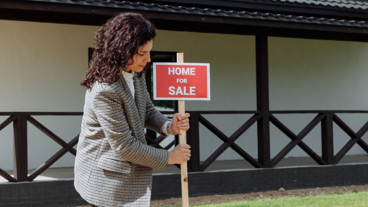 Woman real estate agent placing a 'Home for Sale' sign on a green lawn in front of a house