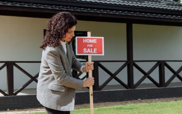 Woman real estate agent placing a 'Home for Sale' sign on a green lawn in front of a house