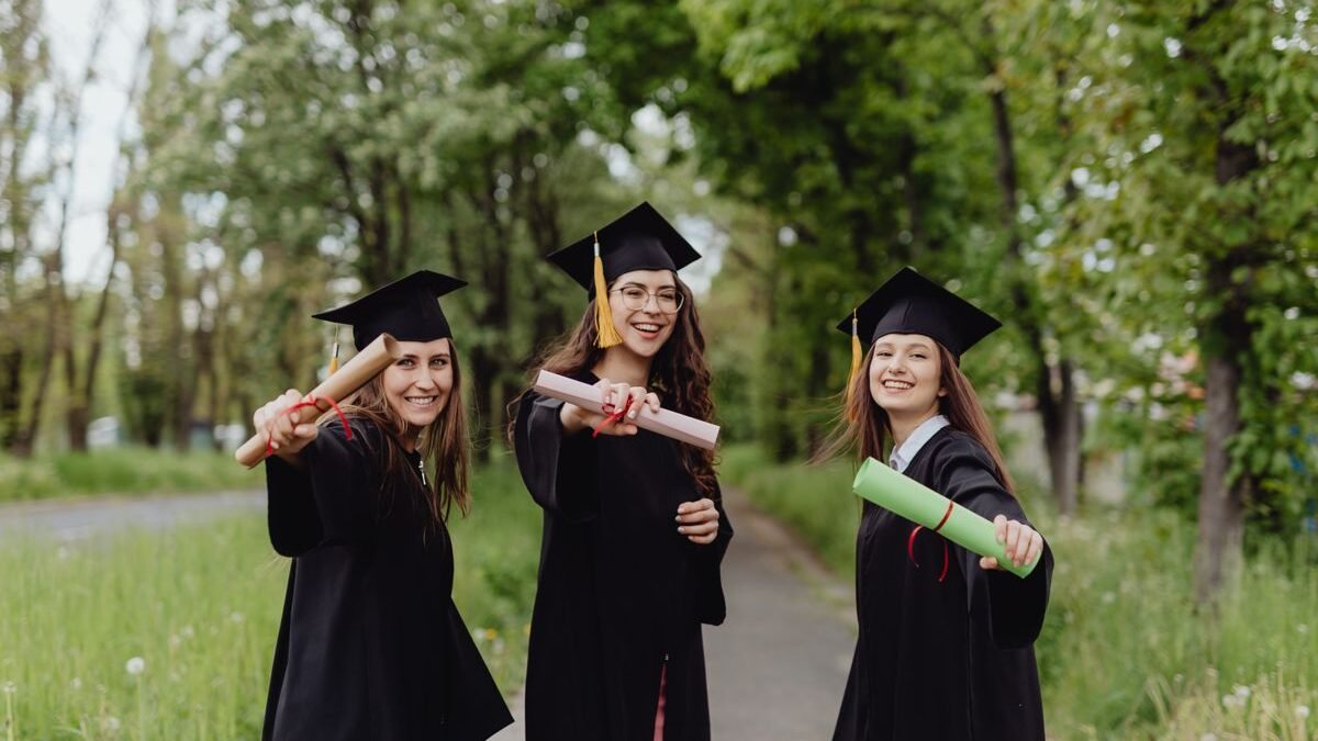 Young women in graduation gowns celebrating with diplomas in a park