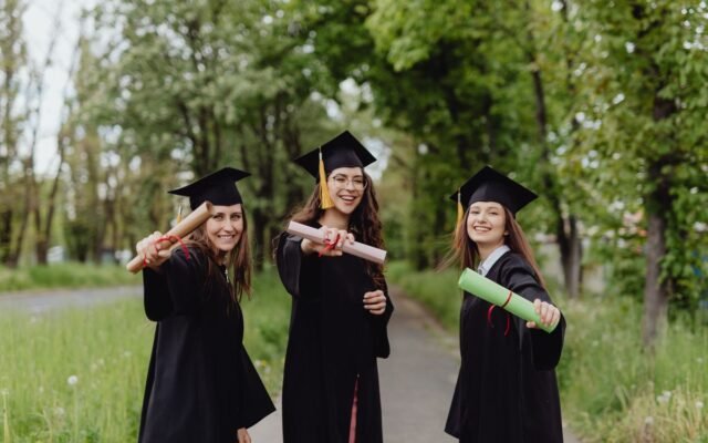 Young women in graduation gowns celebrating with diplomas in a park