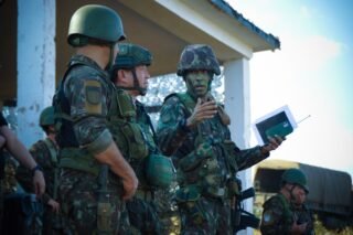 Group of soldiers in camouflage attending a briefing outdoors with tactical gear and helmets