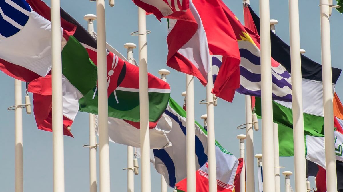 Colorful international flags waving on flagpoles against a clear blue sky