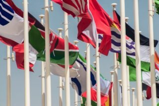 Colorful international flags waving on flagpoles against a clear blue sky
