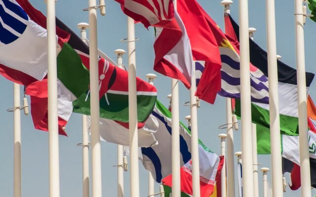 Colorful international flags waving on flagpoles against a clear blue sky