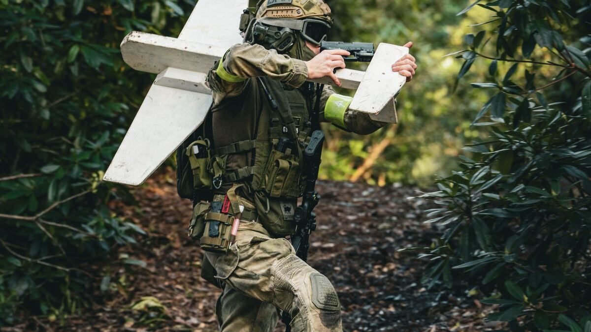 A soldier in camouflage gear carrying a drone in a dense forest setting